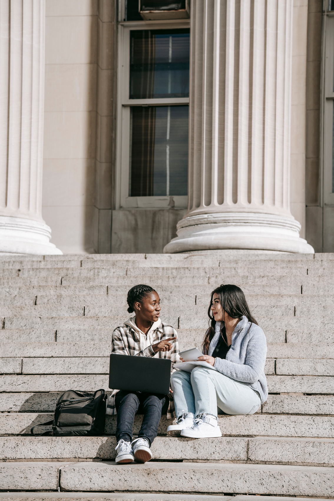 two people sitting on the steps of a building with a laptop